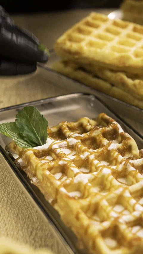 Confectioner working in Bakery. Chef decorated sweet waffles puts mint leaf Stock Footage 319021159