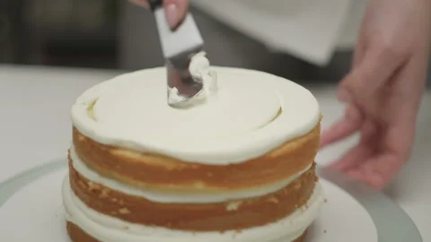 Confectioner's hands decorating rotating cake of three layers using pastry knife Stock Footage 170248353