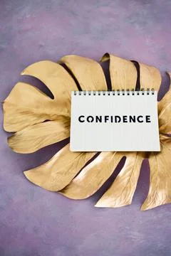 Confidence notepad on top of golden leaf on pink background, psychology and a Stock Photos