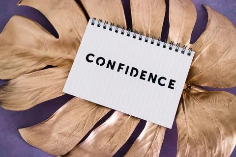 Confidence notepad on top of golden leaf on pink background, psychology and a Stock Photos