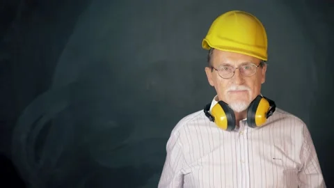 Confidence senior engineer with thumb up wearing a safety helmet over a grey bac Видео 133257459