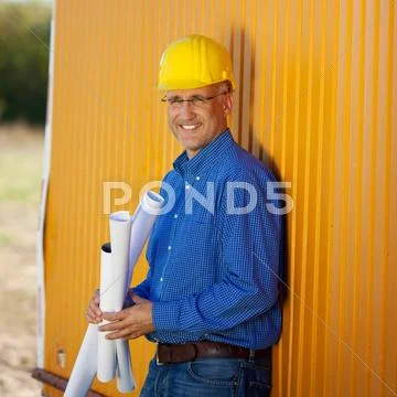 Confident architect holding blueprints while leaning on trailer Stock Photos