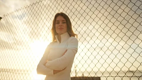 Confident athlete posing with folded arms against chain link fence at sunset Stock Footage 309939526