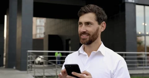 Confident bearded man browsing internet on modern smartphone while standing near Stock Footage 140684651