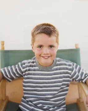 A confident boy sitting in a folding director's chair, smiling a toothy smile. Stock Photos
