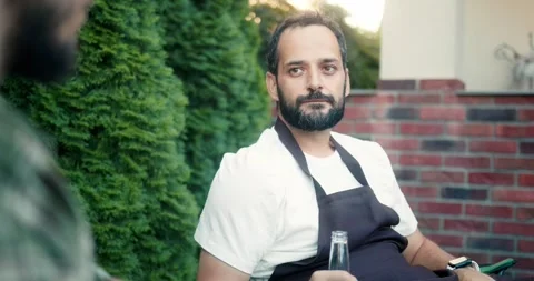 Confident brunette guy in a black apron communicates with his friend and smokes Stock Footage 283830464