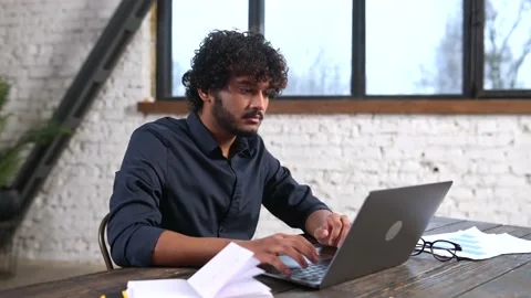 Confident concentrated Indian freelancer guy working on laptop at home office, Video stock 182423883