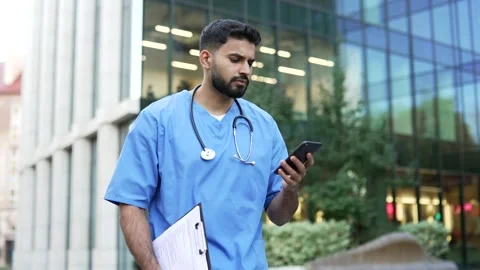 Confident doctor in blue coat using mobile phone while walking outside near  Stock Footage 304588810