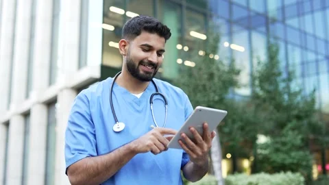 Confident doctor in blue coat using digital tablet standing outside near  스톡 동영상 344434756