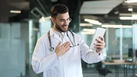 Confident doctor talking on video call using digital tablet in hospital clinic.  스톡 동영상 343355077