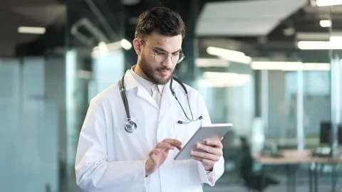 Confident doctor in white coat using digital tablet standing in hospital clinic. Stock Footage 300783344