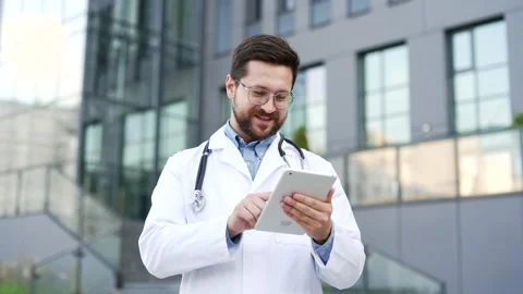 Confident doctor in white coat using digital tablet while standing outside near  Stock Footage 308098938