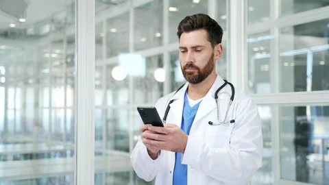 Confident doctor in white coat using mobile phone while standing at workplace Stock Footage 326897831