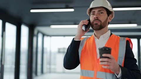 Confident Engineer in Hardhat Talks on Smartphone and Holds Coffee at Stock-Footage 307920165