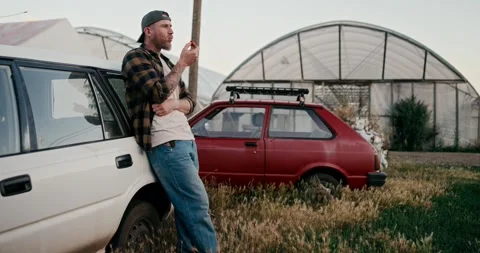 Confident farmer guy in a cap leans on a white car and tries the tomato harvest Stock-Footage 285029509