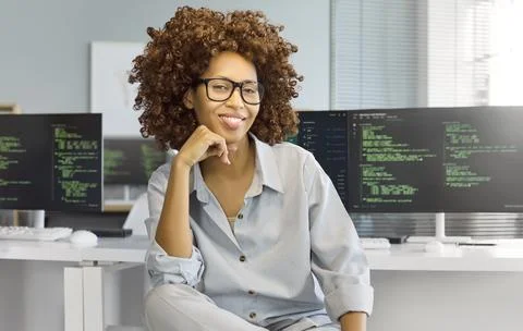 Confident female programmer at computer in modern office, coding on dual screens Stock Photos