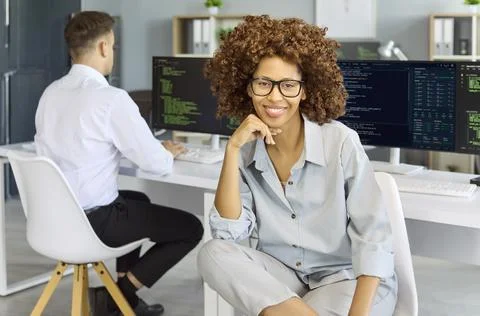 Confident female programmer portrait with code monitors in contemporary office Foto stock