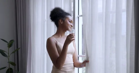 Confident female pulling curtain while holding glass water enjoying fresh Stock-Footage 334930908