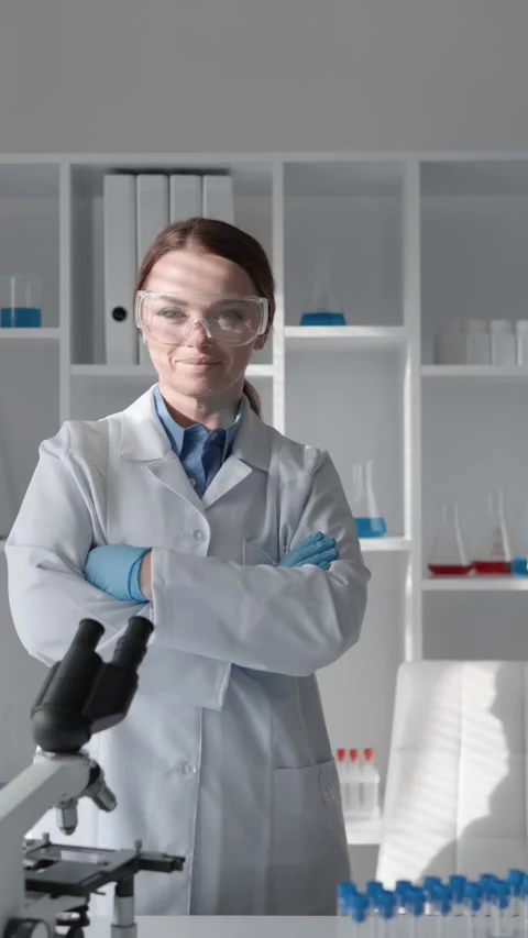 Confident female scientist in white lab coat and safety glasses stands with arms Stock Footage 340923211