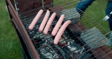 Confident guy in a black apron puts pink sausages on a barbecue grill during a Stock Footage 283832125
