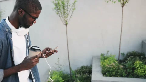 Confident guy climbing steps writes message on phone. Young African American is Stock Footage 139306213