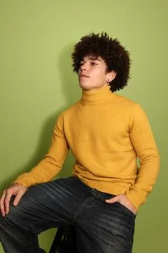 Confident Hispanic guy sitting on stool in green studio Stock Photos