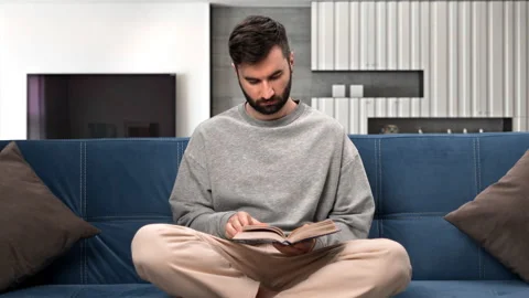 Confident Hispanic man reading interesting paper book sitting on comfy couch at Stock-Footage 229715069