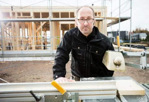 Confident Male Carpenter Using Table Saw To Cut Plank Foto stock