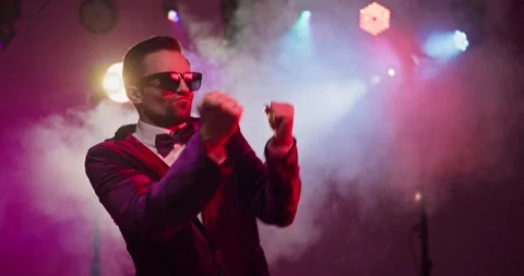 Confident male dancer in sunglasses performs on stage with vibrant lights and Stock Footage 327955513