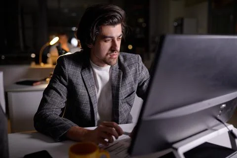 Confident Male Programmer Working on Computer at Night. Table Light Turned On. Stock-Fotos