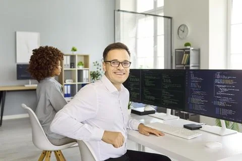 Confident male software developer coding at dual monitors in modern office Fotos Stock
