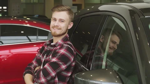Confident man giving a thumbs up while leaning on a sleek new car at the Stock Footage 311939140