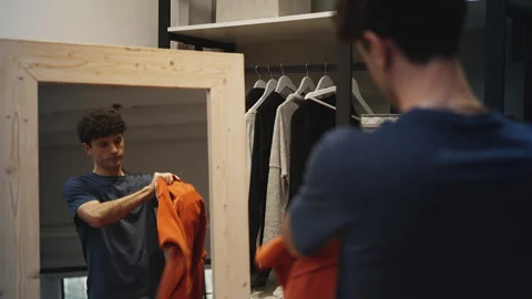 Confident man preparing for a date, putting on orange jacket in wardrobe Stock Footage 337908237