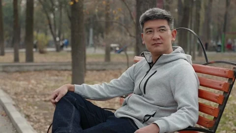 Confident man sitting on a park bench during an autumn day Stock Footage 321768177