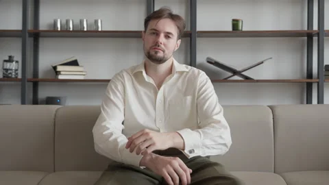 Confident Man Sitting On Sofa, Looking Thoughtful, Casual Home Interior Setting Stock Footage 303759823