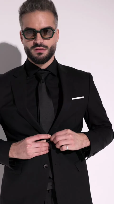Confident man in sunglasses is buttoning his jacket and posing with hands in Video stock 321345940