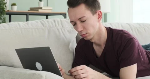 Confident Man Typing on Laptop While Lying on Sofa Stock Footage 250030242