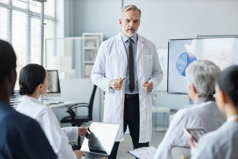 Confident mature male general practitioner in lab coat making speech Stock Photos