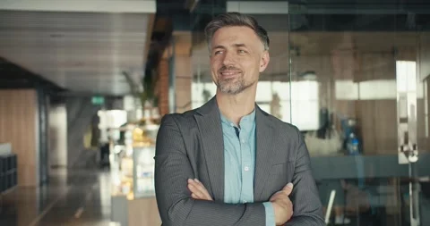 A confident middle-aged man with gray hair and a gray suit poses against the Stock Footage 243453516