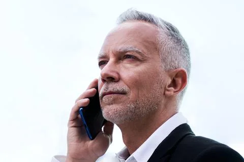 Confident middle aged man using mobile to work, standing outdoors with white Stock Photos