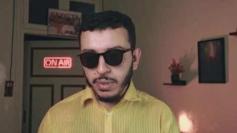 Confident Vlogger in Sunglasses Speaking to Camera, Warm Neon Room Video stock 318593101