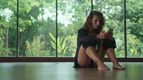 Confident woman sitting on floor in empty room switching music on smartphone Stock Footage 246360474