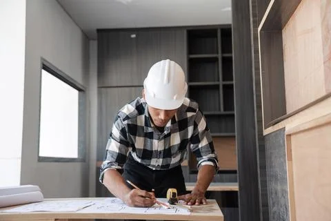 Confident Young Engineer Planning Work with Blueprints in Modern Office Foto stock