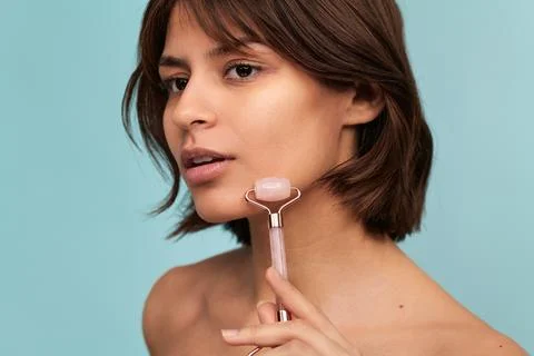 Confident young Hispanic lady using facial roller during skincare procedure Stock Photos