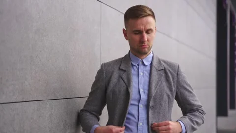Confident young man buttoning his jacket, standing outdoors. Slow motion 動画素材 255896875