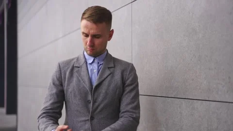 Confident young man buttoning his jacket, standing outdoors. Real time 動画素材 256345516