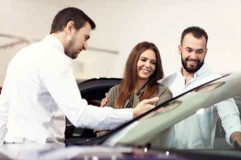 Confident young salesman explaining car features to the young attractive owners Stock Photos