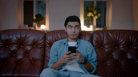 Confused Asian guy thinking about what to write up in chat on mobile phone. Stock Footage 105752741
