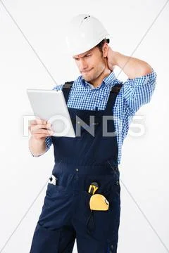 Confused builder in helmet scratching his head and holding tablet Stock Photos