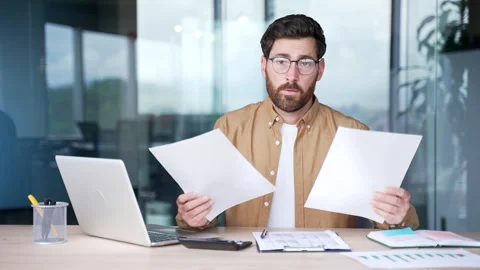 Confused businessman having difficulty with paperwork sitting at a desk at work Stock Footage 316679253